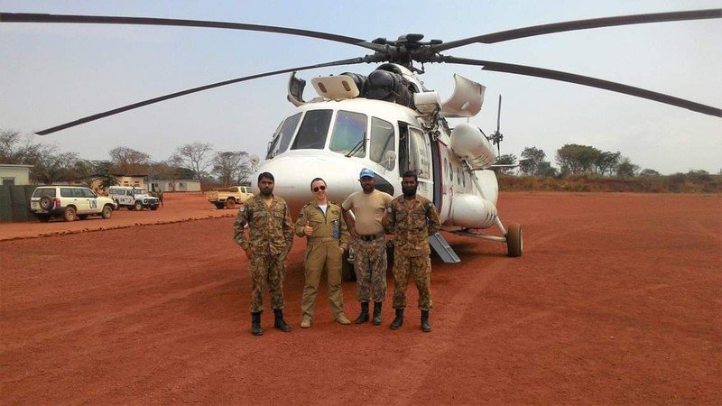 Pelican Flight School graduate standing with UN crew near a helicopter.